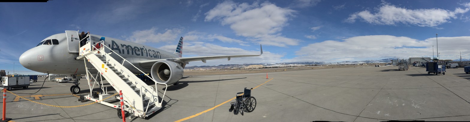 American Airlines aircraft on the tarmac with mobile boarding stairs and empty wheelchair under a blue sky with scattered clouds.