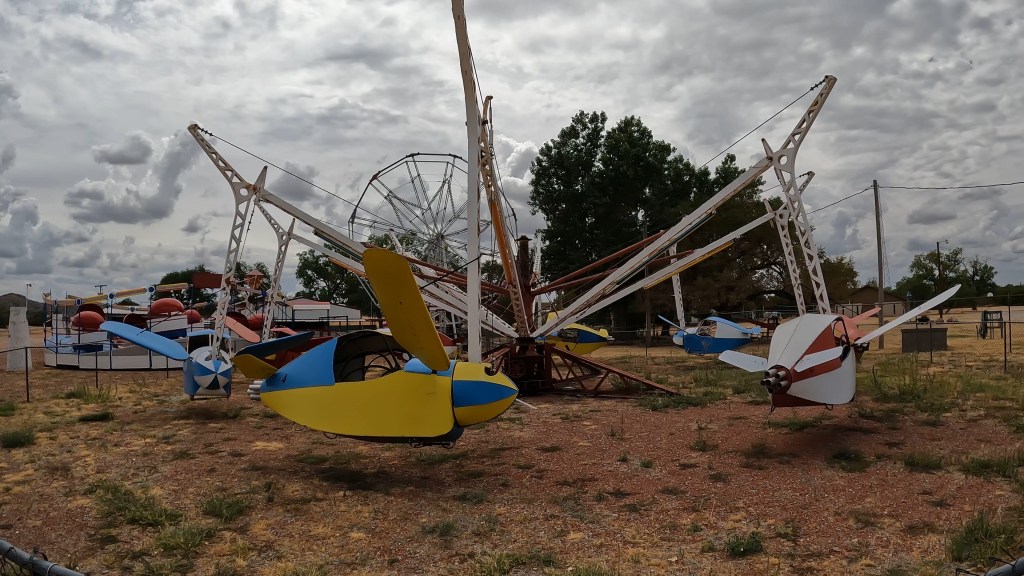 A vintage airplane amusement park ride sits motionless in the arid Oklahoma Summer Heat.
