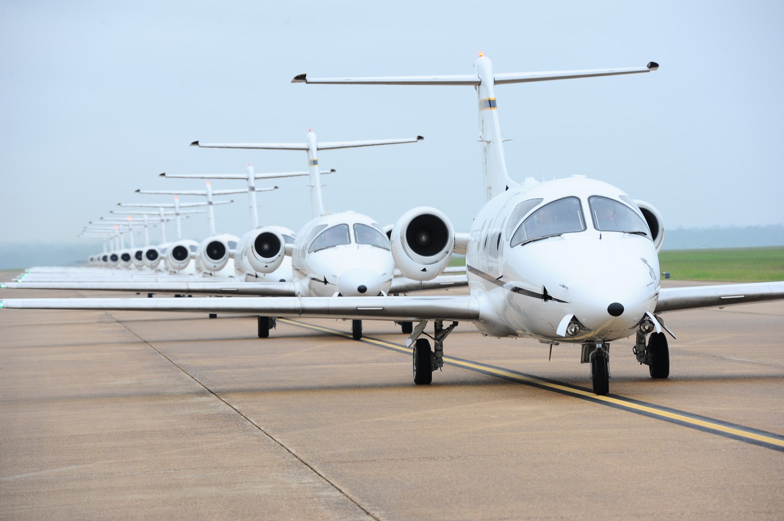 Row of white business jets taxiing on the runway in formation, showcasing precision and readiness on a cloudy day.
